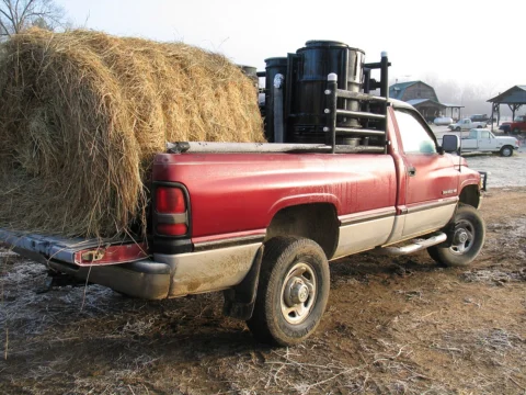 A pickup carrying hay with wood-gas equipment behind the cab.