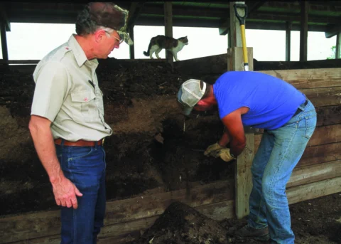 Two people examining a poultry-litter composter.