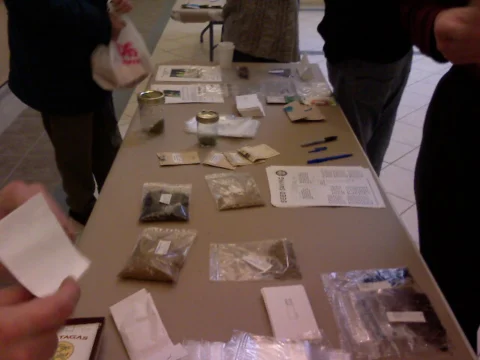 People examining packets and labels on a seed-exchange table.