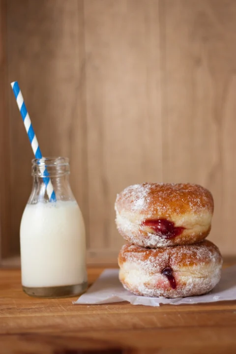 A glass bottle of milk beside two doughnuts.